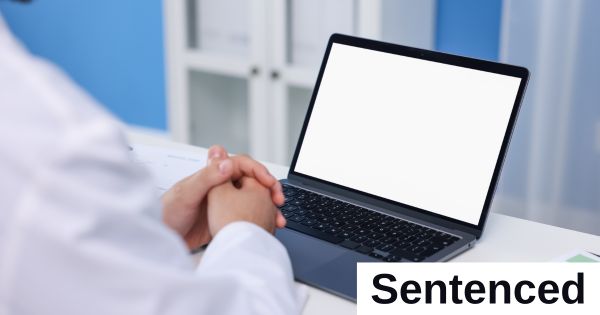 A person sits with their hands folded in front of a computer screen.