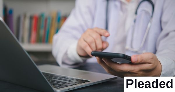 A doctor taps his phone while sitting in front of a computer.