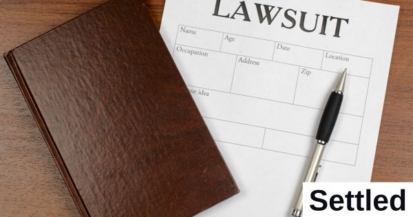A tablet, a paper with the word "Lawsuit," and a pen sit on a table.