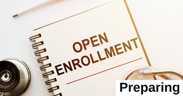 A notebook with the words "Open Enrollment" sits on a desk.