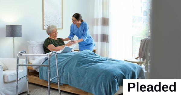 A care worker gives a woman, who is in bed, a glass of water.