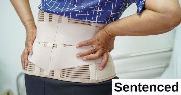A person places a hand on a back brace that they're wearing.