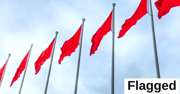 Seven red flags stand against a backdrop of a blue sky.